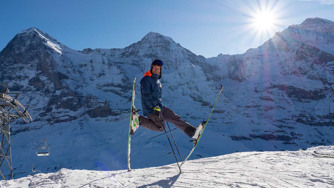 Skifahrer macht ein Kunststück und steht auf zwei Skiern vor Bergpanorama