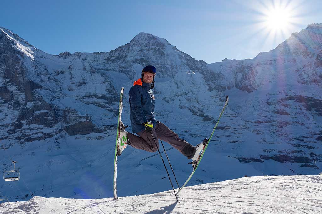 Skifahrer steht lässig im Schnee vor Bergpanorama und Sonnenschein