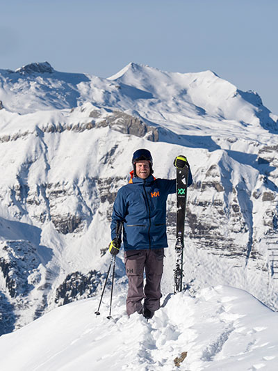 Julian Witting steht auf Berggipfel im Winter mit Skiern in der Hand